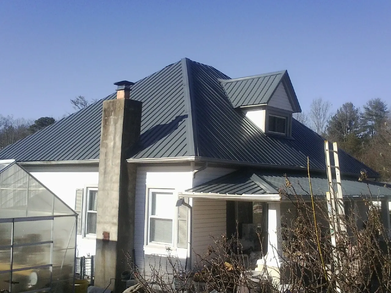 Dark blue standing seam metal roof on a white farmhouse with dormer — Slate & Tile Roof Repair by Roofing Brothers in Porter Ranch