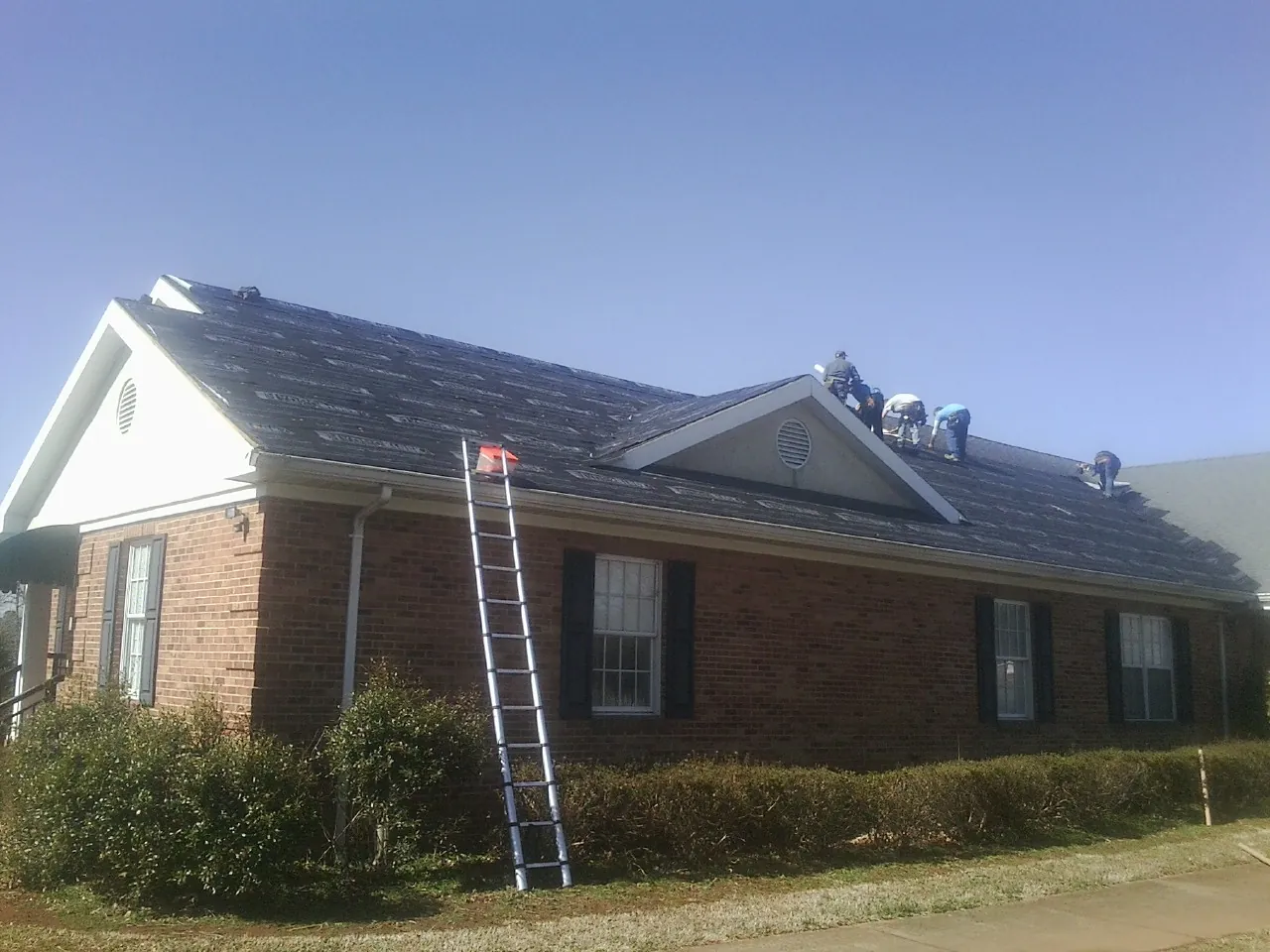 Crew tearing shingles off a brick ranch roof with a ladder set — Metal Roof Repair work by our crew in Porter Ranch