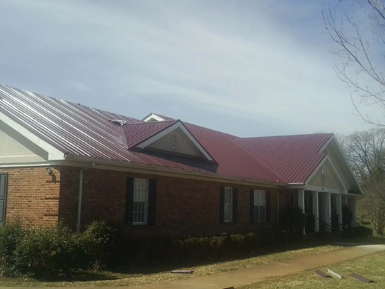 Red metal roof with gabled entries on a long brick building, from a Hail Damage Roof Repair job in Porter Ranch