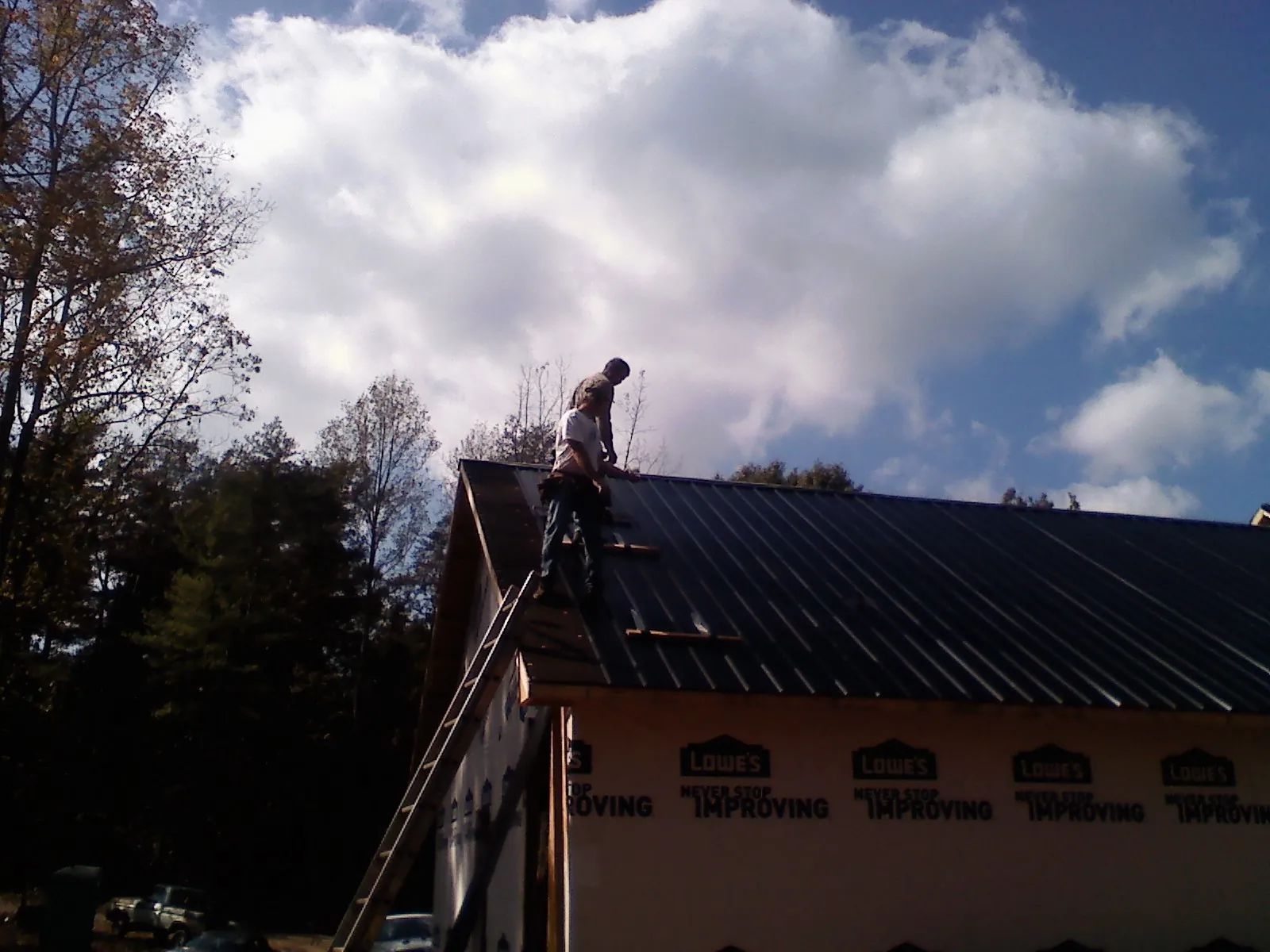 Roofer fastening dark metal panels high against a cloudy sky, from a Roof Inspection job in Porter Ranch